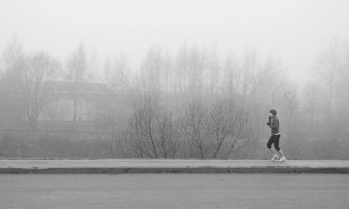 Side view full length of man jogging on sidewalk during foggy weather
