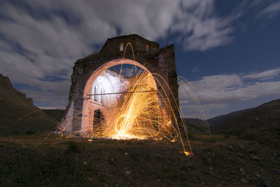 Illuminated ferris wheel on mountain against sky at night