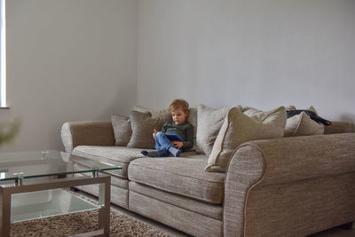 Boy sitting on sofa at home and playing tablet