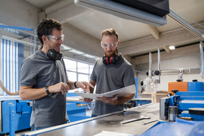 Two male carpenters talking over documents in production hall