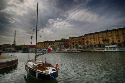 Boats in harbor against cloudy sky