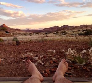 Low section of person legs on land against sky during sunset