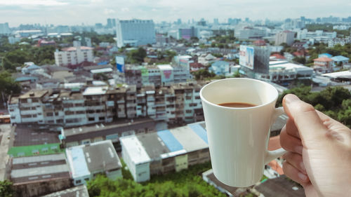 Close-up of hand holding coffee cup against cityscape