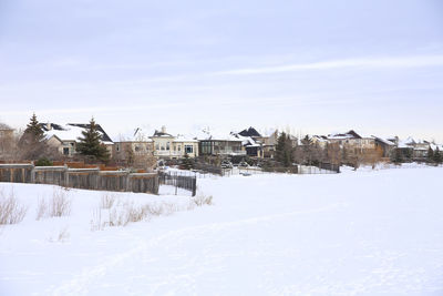 Snow covered houses by buildings against sky