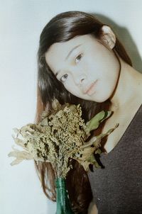 Portrait of teenage girl holding plant against wall