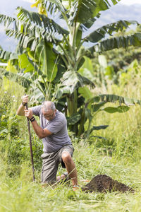 Elderly man digging deep hole with shovel outdoors.