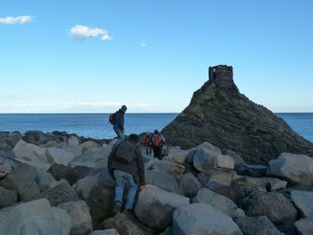 People walking on rocks at sea shore against sky