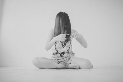 Full length of woman cutting her hair against white background