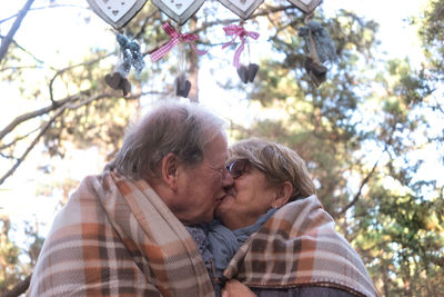 Low angle view of couple kissing against trees