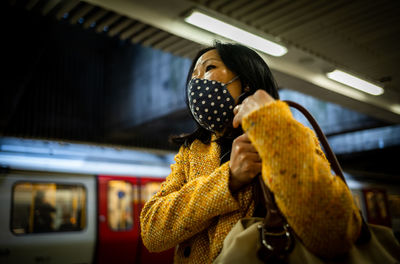 An asian woman from vietnam wearing a face mask waits for a train on the london underground.