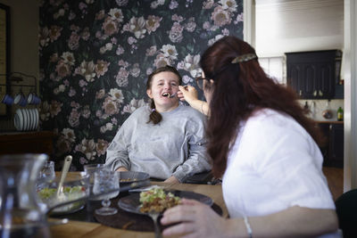 Mother feeding disabled teenage daughter in wheelchair at table