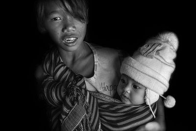 Portrait of girl carrying sister against black background