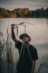 Man wearing sunglasses standing by lake against sky during sunset