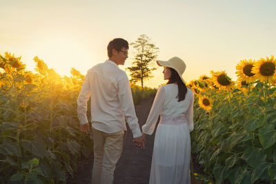 Friends standing on field against sky during sunset