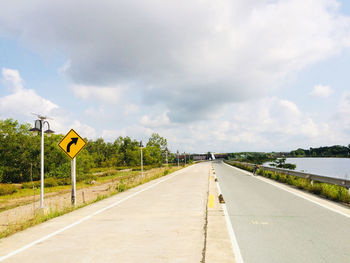 Empty road leading to sign against sky