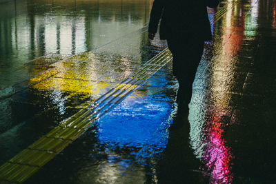 Low section of person walking on wet road at night