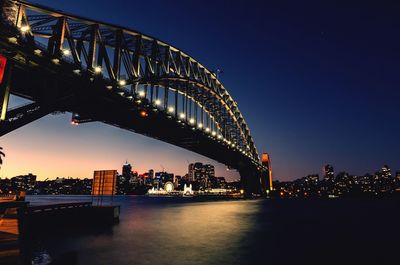 Illuminated bridge over river against sky in city at night