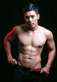 Portrait of shirtless young man against black background