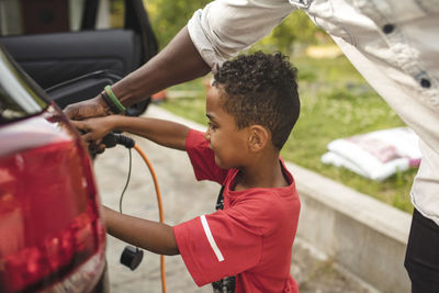 Midsection of man assisting son in charging electric car on driveway at front yard