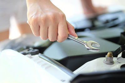 Cropped hand of mechanic repairing car engine with wrench