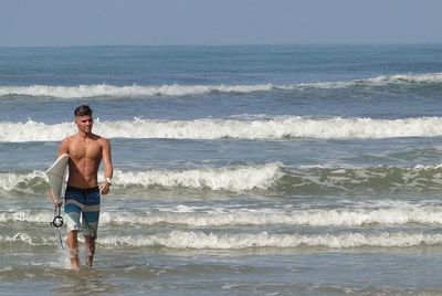 Full length portrait of shirtless man standing at beach