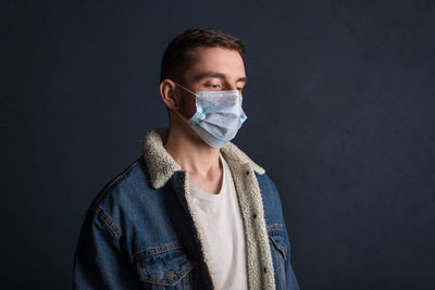 Portrait of a young man wearing a medical mask on a dark gray background to protect and stop viruses