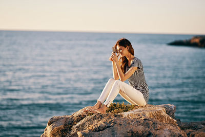 Woman sitting on rock by sea against sky