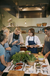 Multiracial students and female chef discussing together during cooking class in kitchen