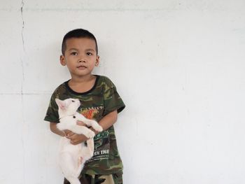 Portrait of cute boy with cat against white wall