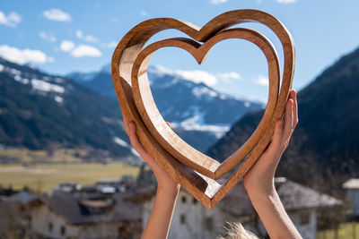 Cropped hands of woman holding heart shape against mountains