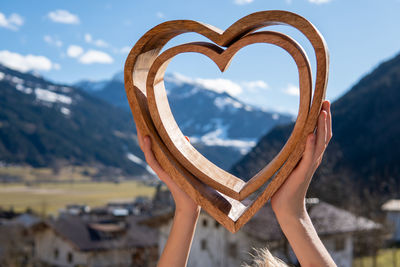 Reflection of woman holding heart shape on mountain against sky