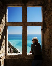 Rear view of woman looking at sea seen through window