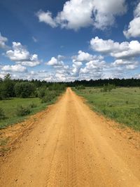 Dirt road amidst field against sky