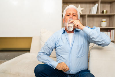 Portrait of senior man using mobile phone while sitting on sofa at home