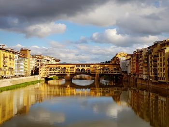 Arch bridge over river by buildings against sky in city