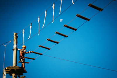 Low angle view of girl hanging on cable against sky