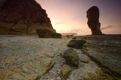 Rock formation on shore against sky during sunset