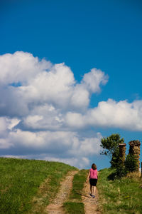 Rear view of woman walking on field against cloudy sky