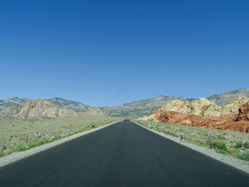 Empty road along landscape against clear blue sky