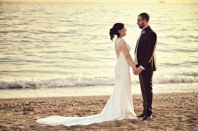 Full length of couple standing at beach during sunset