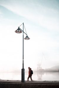 Man standing by street light against sky
