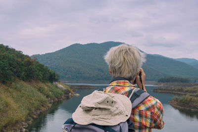 Rear view of man photographing lake against mountains