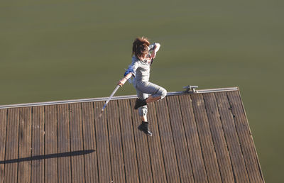 Female athlete performing martial arts stunt with sword while jumping on promenade during sunny day