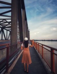 Rear view of woman standing on bridge against sky