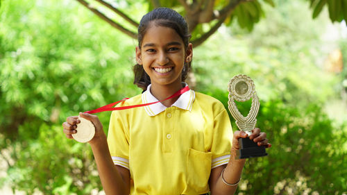 Portrait of a happy school girl wearing school uniform celebrating victory trophy in hand.