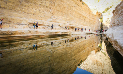 People walking by mountain with reflection in river