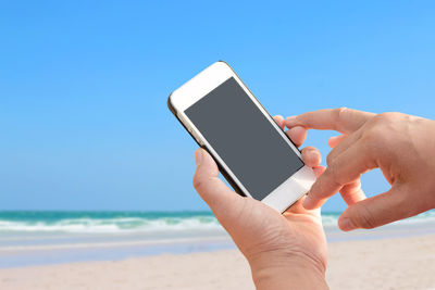 Cropped hands of woman using phone at beach