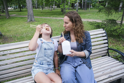 Mid adult mature woman and teenage girl on a summer day in the park has lunch with noodles wok