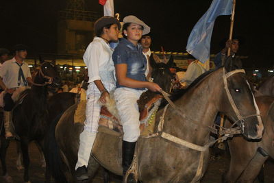 Full length of young woman sitting with horse in background at night