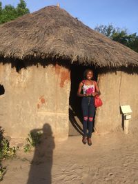Smiling young woman standing at doorway of thatched roof hut in makumbusho